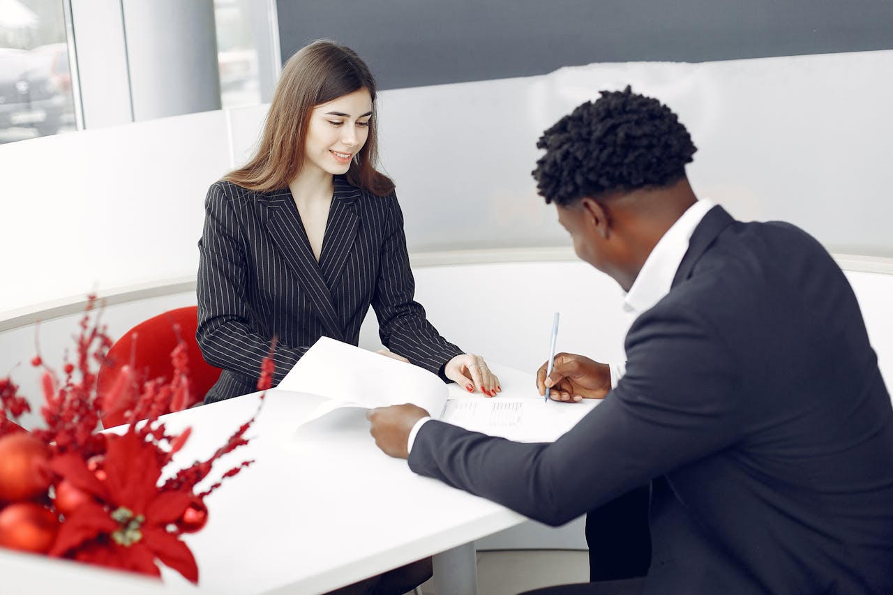 Positive stylish multiethnic buyer in formal classy suit and agent signing papers in modern light creative office in daylight and smiling happily